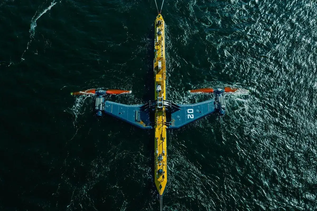 Podwodna turbina wykorzystująca energię pływów, z charakterystycznymi żółto-niebieskimi elementami i pomarańczowymi śmigłami, zanurzona w ciemnych wodach oceanu.