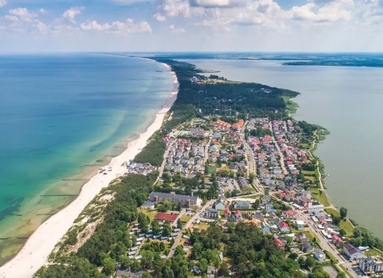 Widok z lotu ptaka na Mielno: plaża, morze, jezioro i zabudowania.