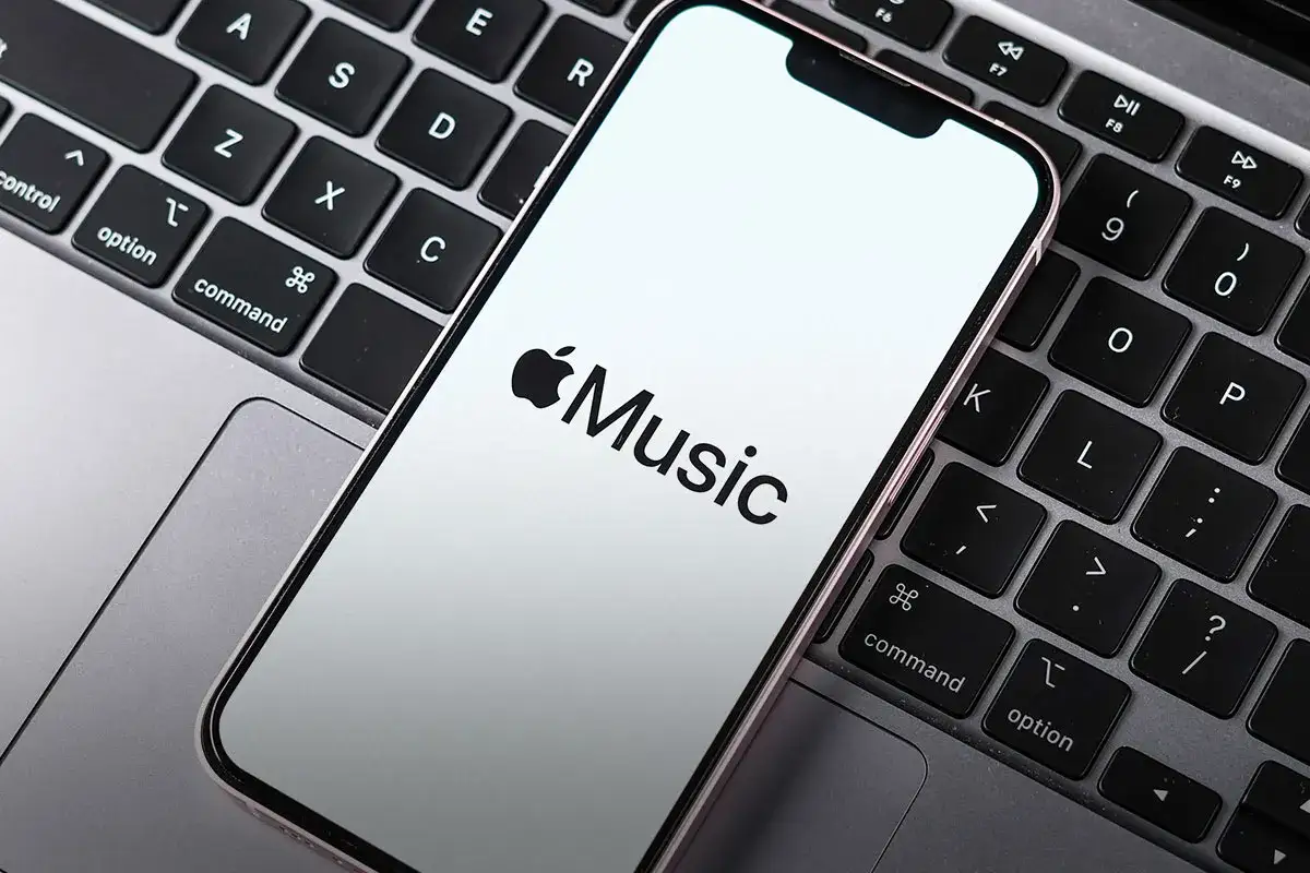 Telefon z logo Apple Music leży na klawiaturze laptopa. Sprawdź aktualną apple music cena.