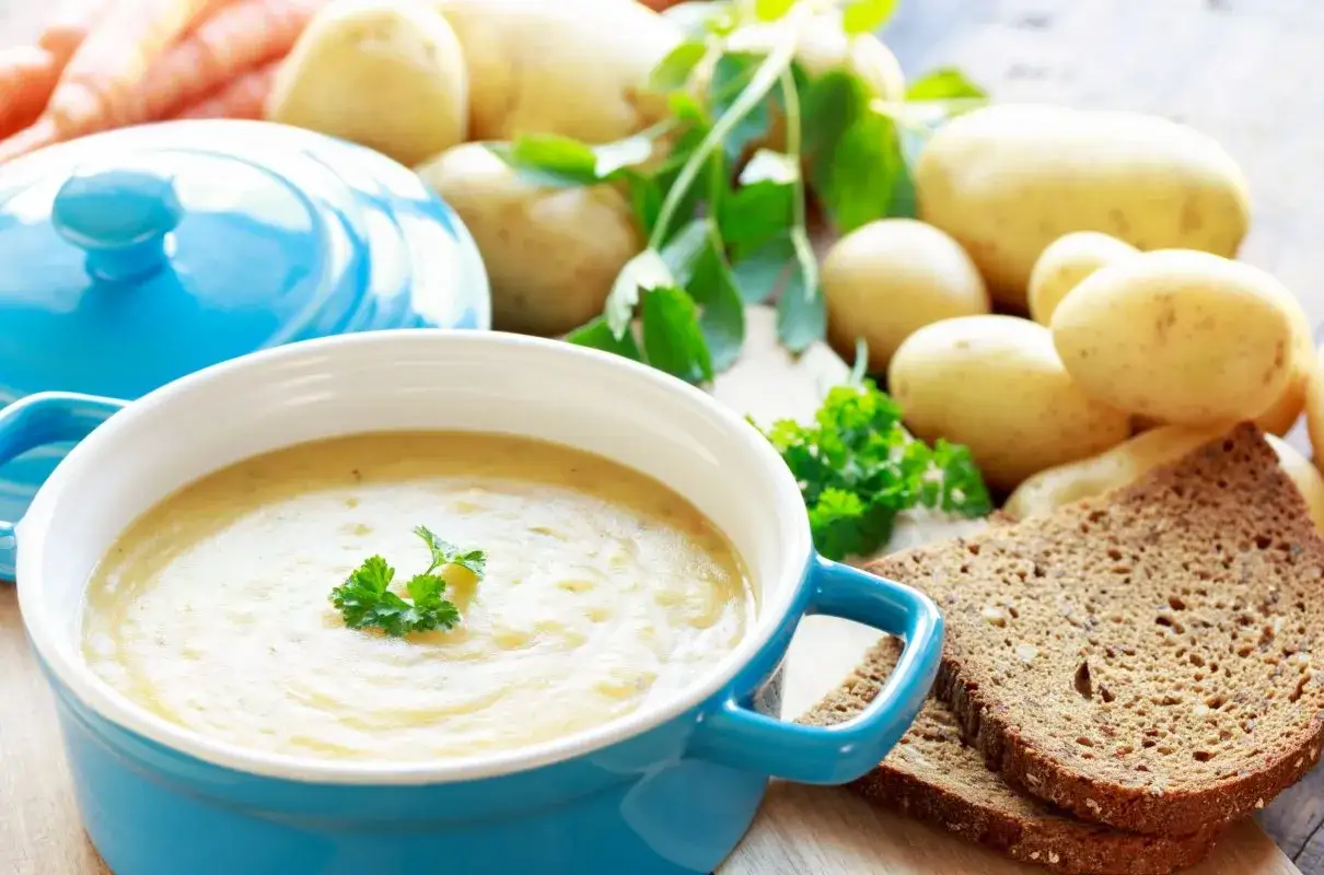 Aksamitna zupa ziemniaczana, przepis babci, z chlebem i świeżymi ziemniakami w tle.