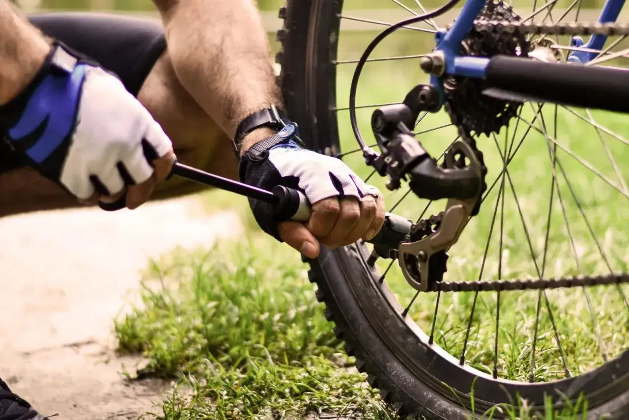 Rowerzysta w rękawiczkach pompuje koło roweru, pokazując, jak napompowac koła na stacji.