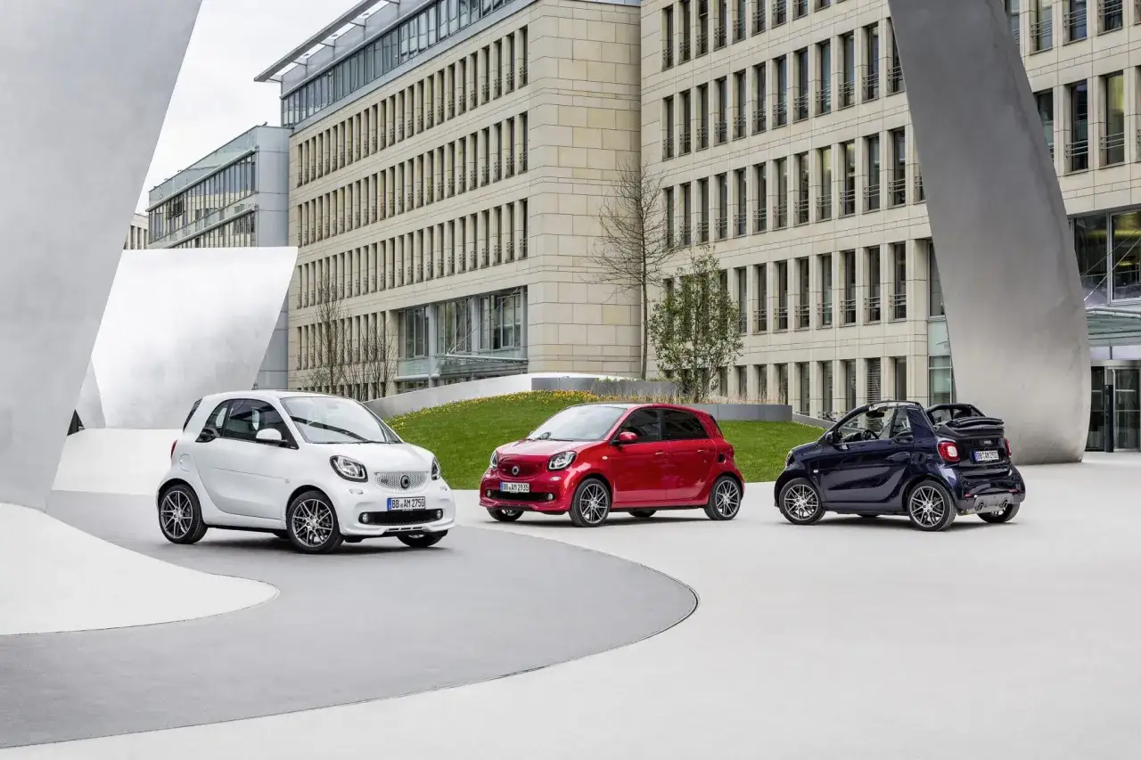 Trzy samochody Smart, w tym jeden w wersji Brabus, zaparkowane przed nowoczesnym budynkiem.
