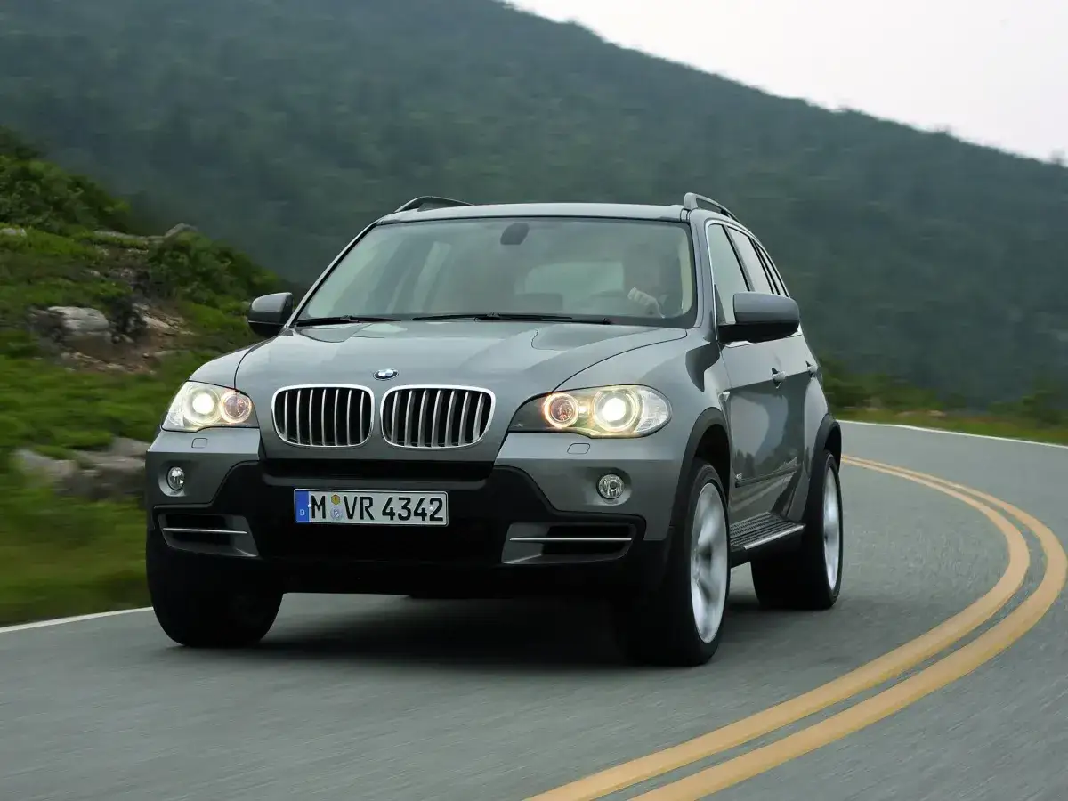 Szary BMW X5 E70 pokonuje zakręt na malowniczej górskiej drodze.