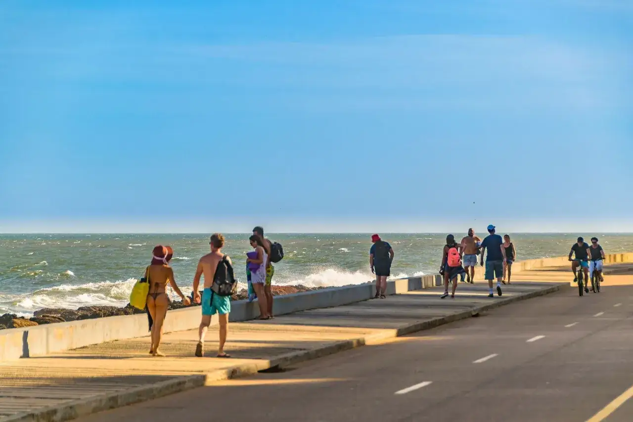 Ludzie spacerują i jeżdżą na rowerach wzdłuż promenady nad oceanem w słoneczny dzień.