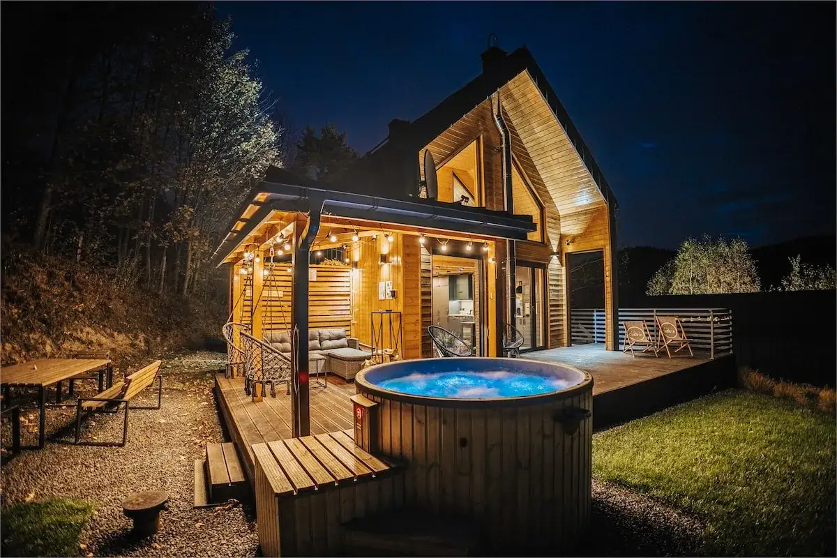 Drewniany domek z jacuzzi i tarasem, idealne miejsce na babia góra noclegi. Oświetlony girlandami, zaprasza do relaksu.