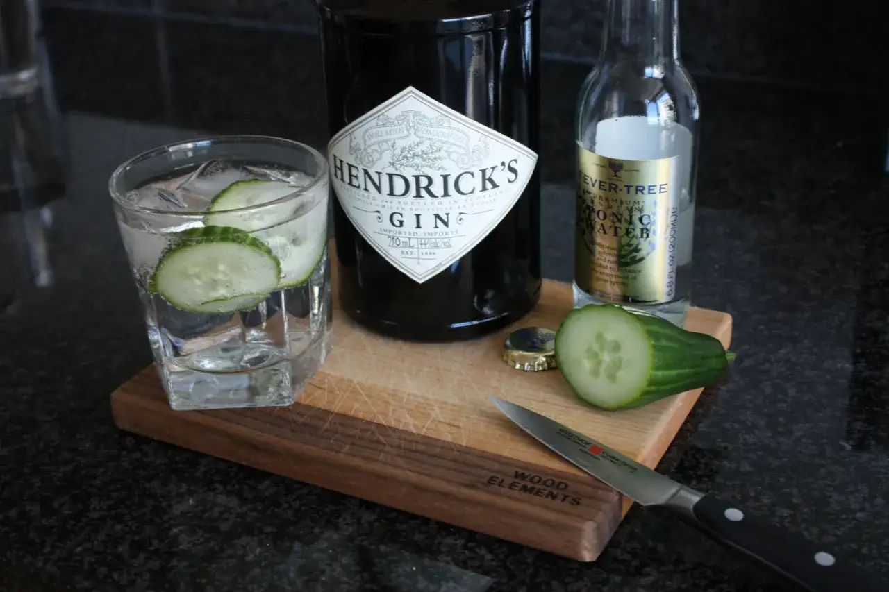 Szklanka z ginem Hendrick's i ogórkiem, obok butelka ginu, Fever-Tree i plasterki ogórka. Idealne składniki do drinków.