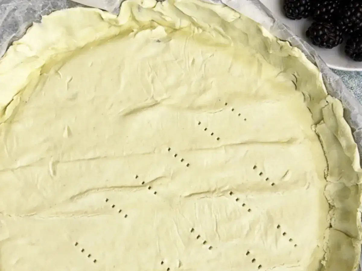 Surowe ciasto na tartę, z widocznymi dziurkami, czeka na wypełnienie. Tarta na kruchym spodzie czy na cieście francuskim?
