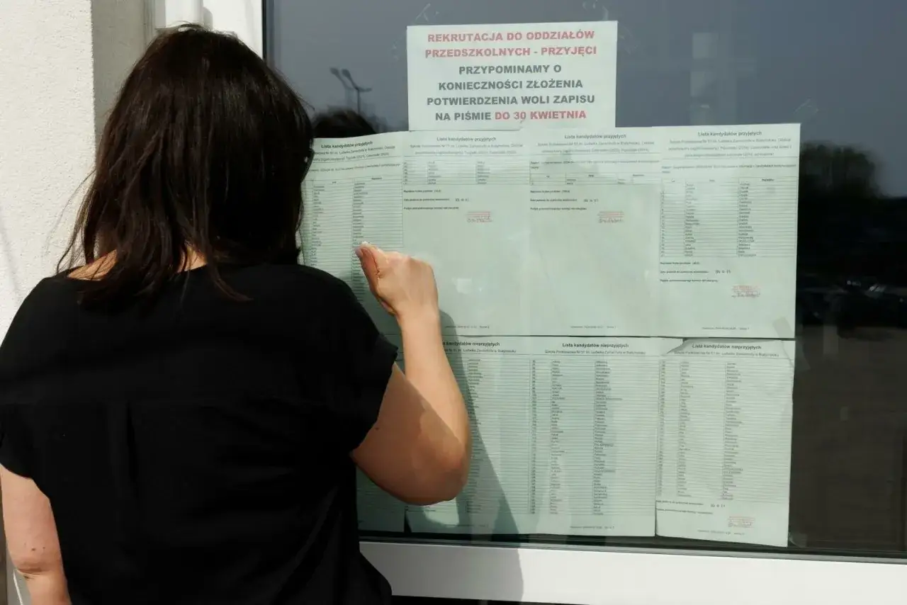 Kobieta sprawdza listę kandydatów, kiedy jest wystawienie ocen. Widać ogłoszenie o rekrutacji do przedszkola.