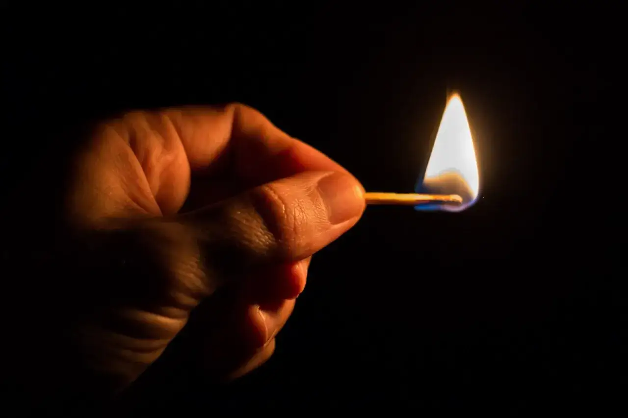 Dłoń trzyma płonącą zapałkę. Czy Polsce grozi blackout? Mały płomień symbolizuje niepewność.