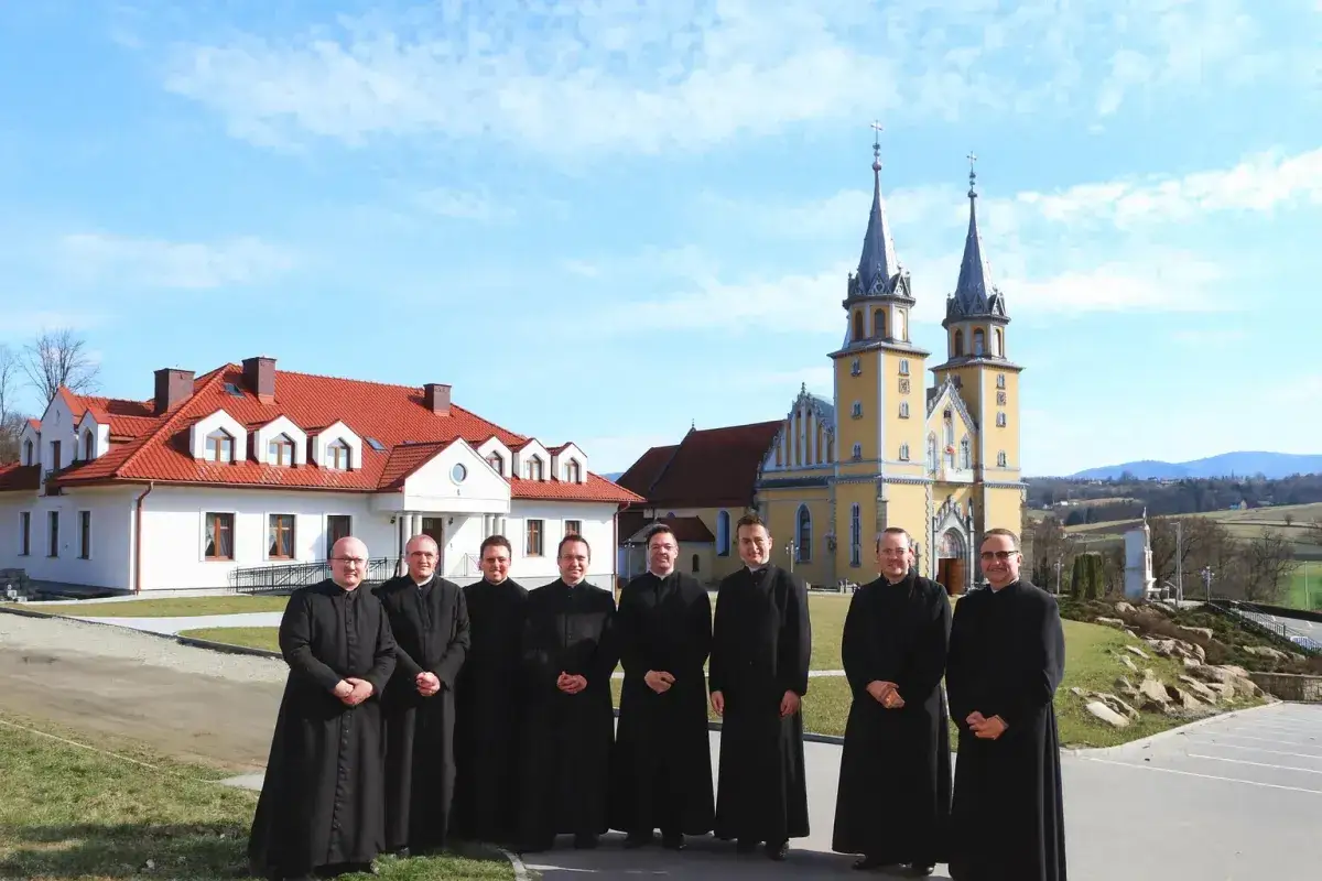 Grupa księży w czarnych szatach przed żółtym kościołem. Czy to miejsce, gdzie zbierany jest podatek na kościół?