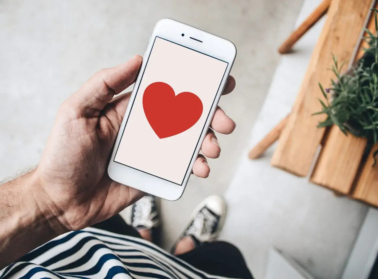 Dłoń trzyma smartfon z czerwonym sercem, symbolizującym co oznacza słowo love.