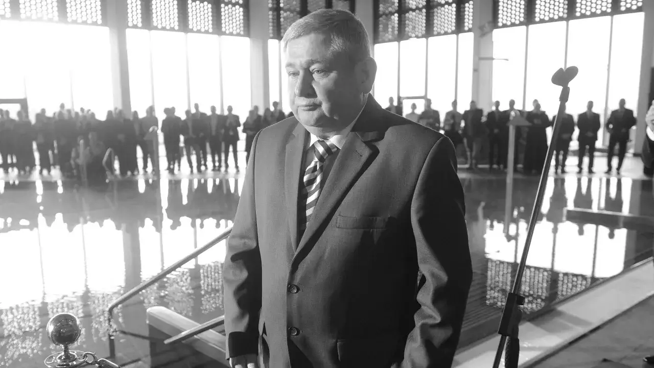 Jan Harhaj, starosta lidzbarski, w garniturze, stoi przed grupą ludzi w jasnym pomieszczeniu.