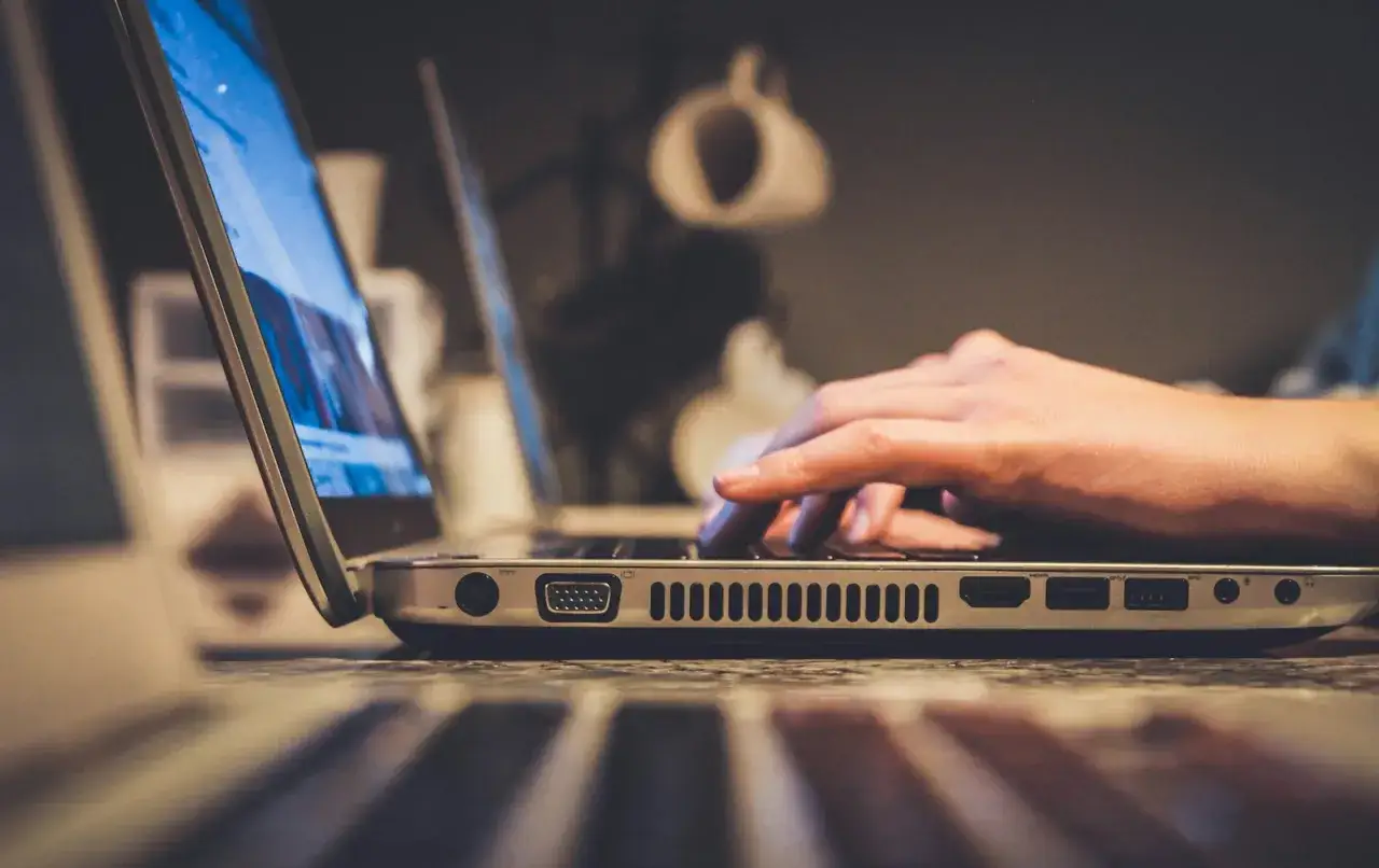 Dłoń pisząca na klawiaturze laptopa, widok z boku.