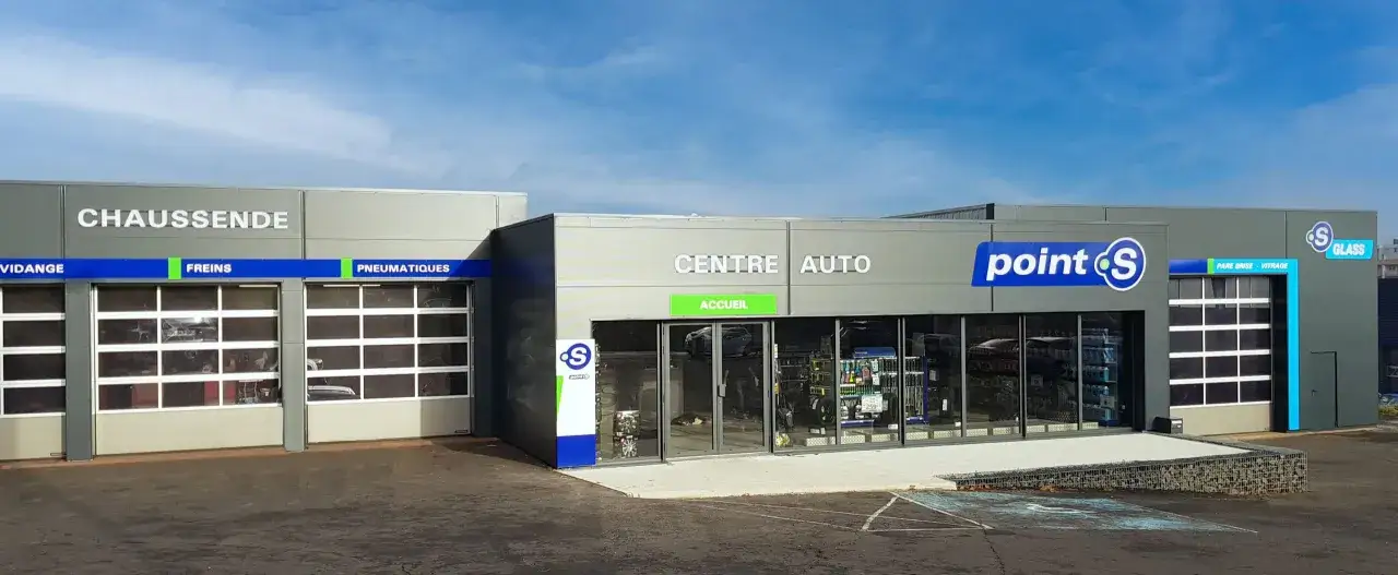 Façade d'un centre auto Point S avec des portes de garage et des panneaux indiquant les services (vidange, freins, pneumatiques, pare-brise).