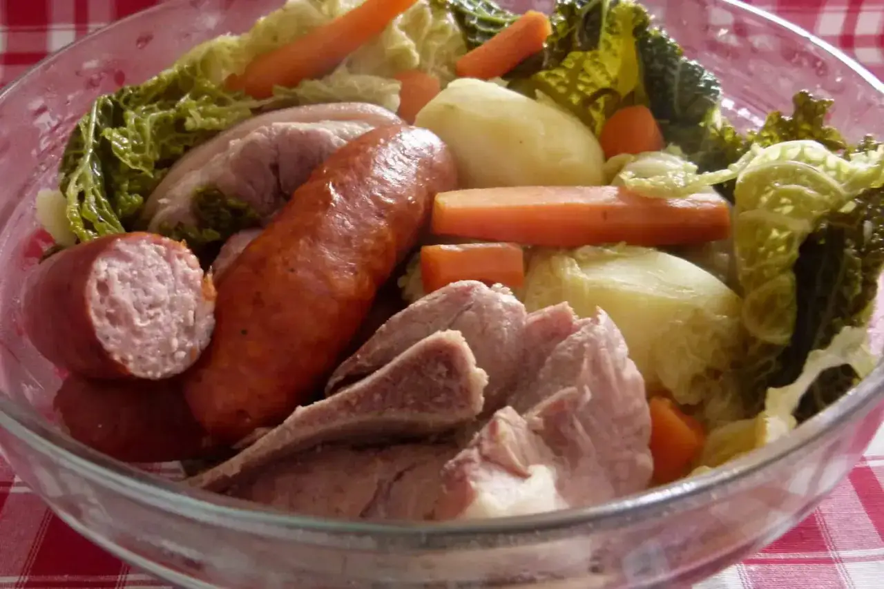 Un plat typique auvergnat : saucisses, porc, pommes de terre, carottes et chou savoyard mijotés dans un grand bol en verre.