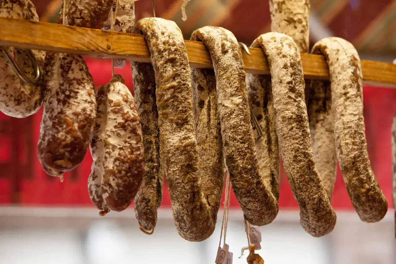 Saucissons secs, une spécialité culinaire auvergnate, pendent sur un support en bois.
