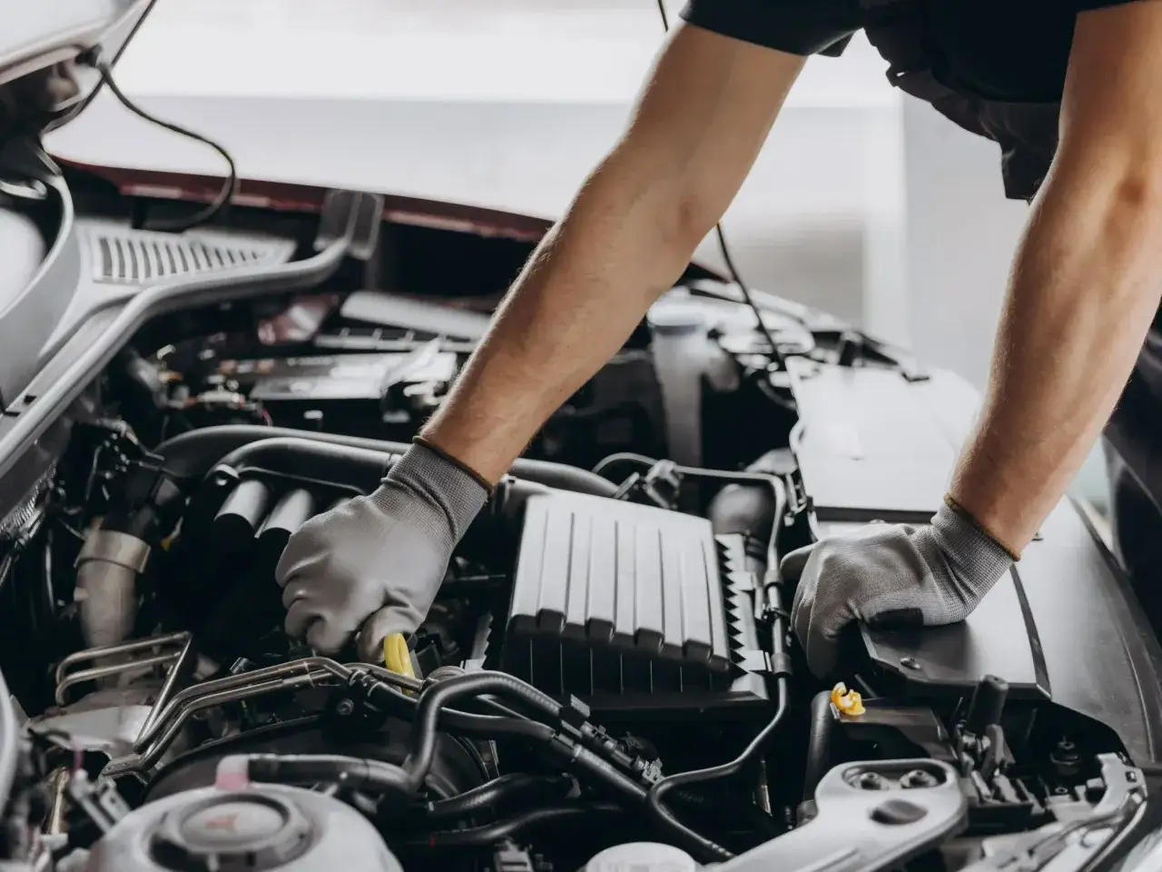 Mechanik w rękawiczkach pracuje przy silniku, dbając o zgodność z normami emisji spalin i tabelą CO2.
