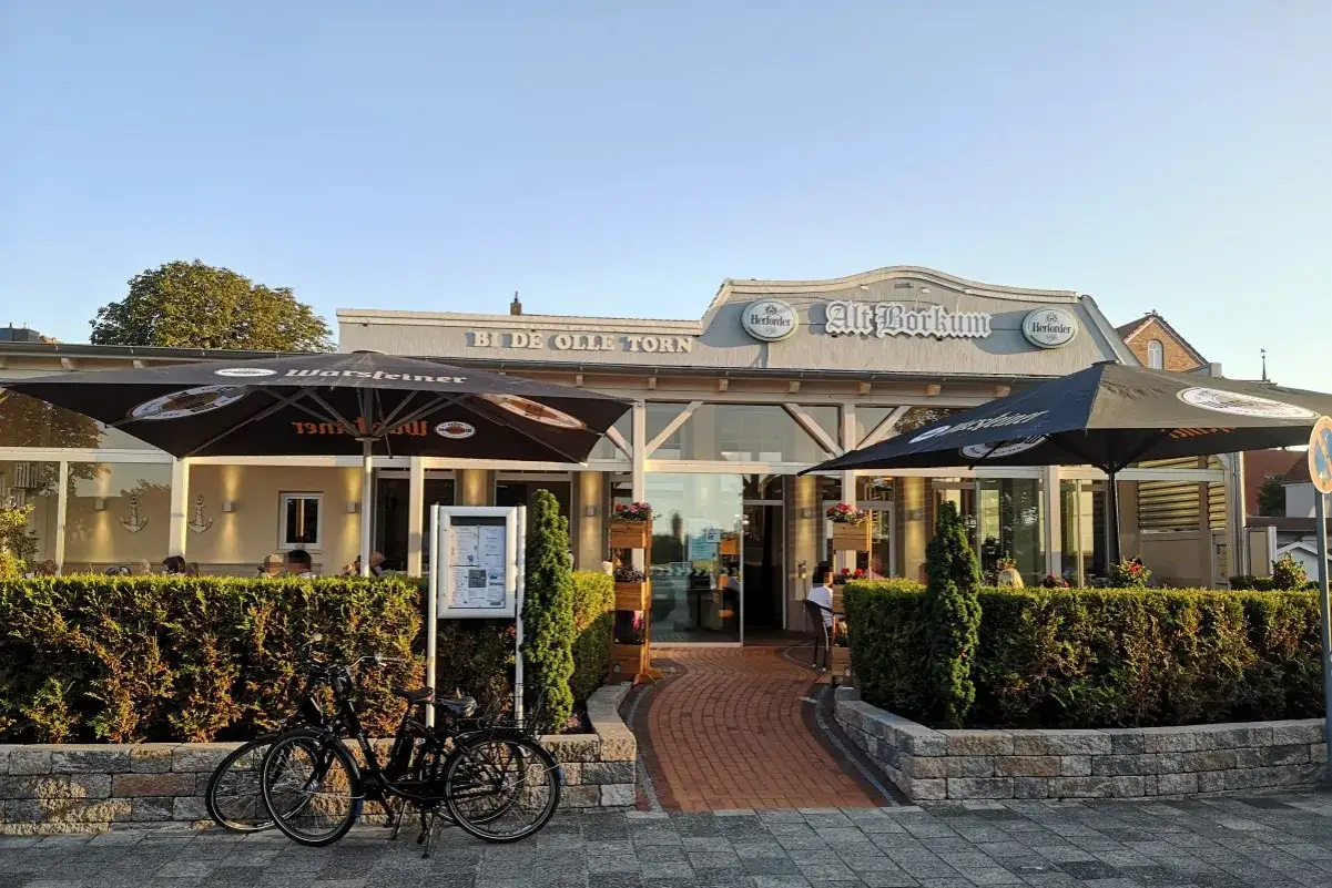 Zwei Fahrräder vor dem Restaurant "Alt Borkum" mit Sonnenschirmen und Büschen.