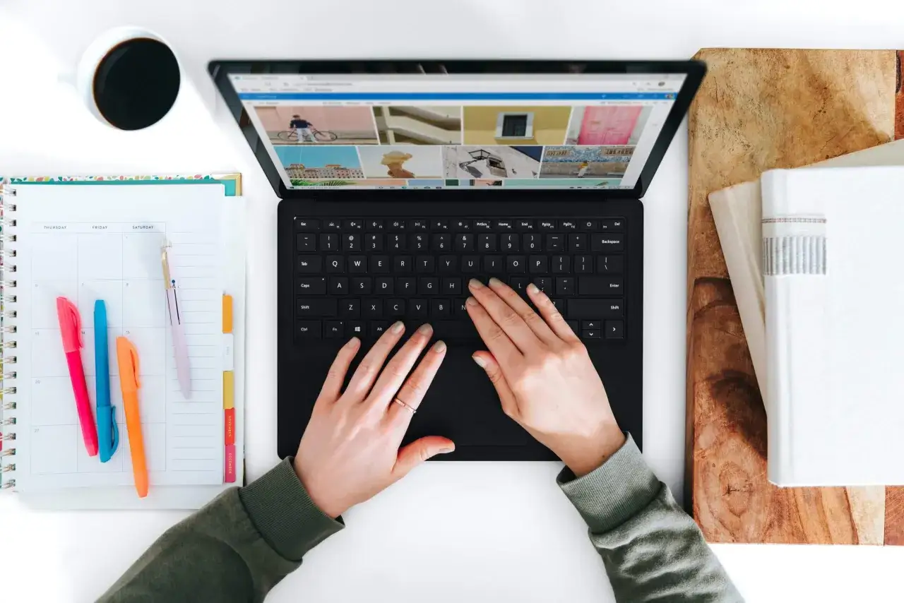 Hände tippen auf einem Laptop, daneben ein Kalender und eine Kaffeetasse.