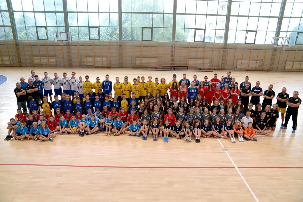 Drużyna Olimp Grodków na hali sportowej. Duża grupa dzieci i młodzieży w strojach sportowych pozuje do wspólnego zdjęcia.