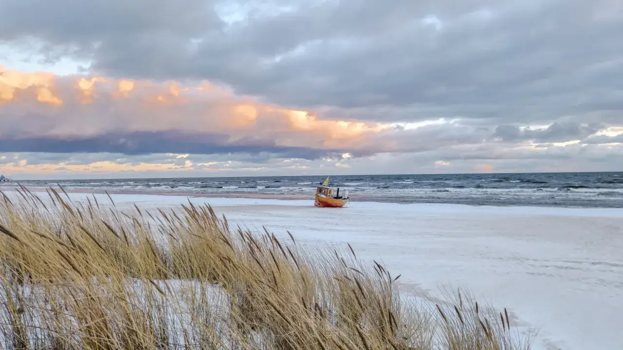 Ein kleines Boot liegt am verschneiten Strand der Ostsee, im Hintergrund die Seebrücke von Ahlbeck.