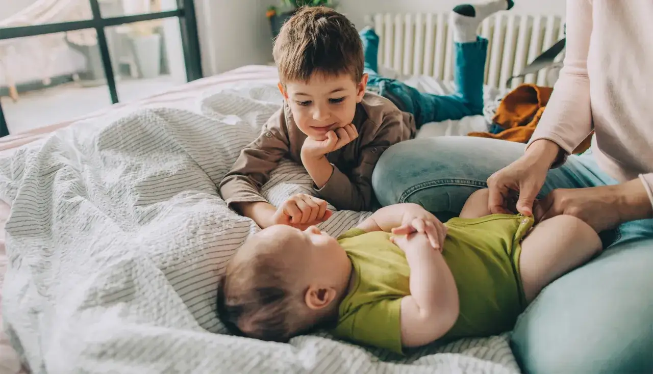 Starszy brat patrzy z czułością na niemowlę. Zastanawiamy się, ile cm rośnie dziecko w ciągu roku, obserwując te małe nóżki.