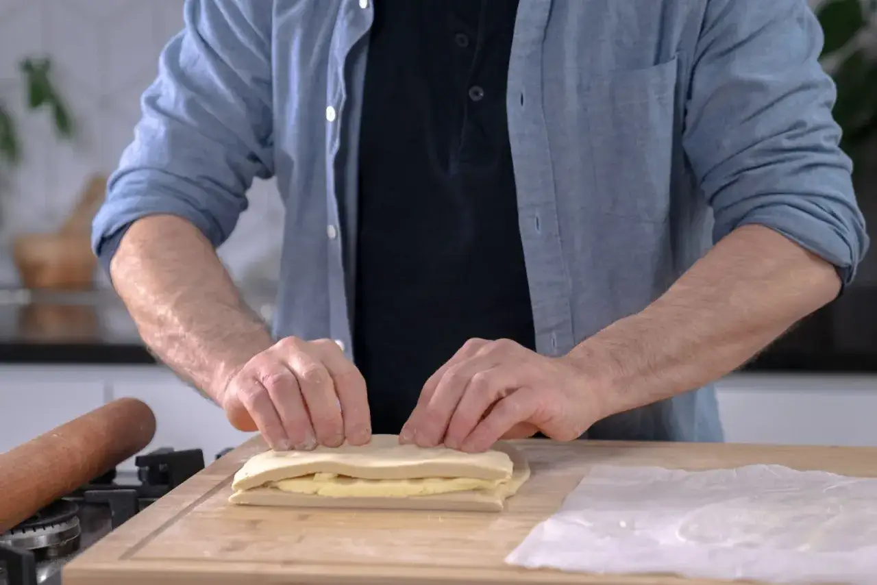 Un homme plie une pâte feuilletée professionnelle sur une planche en bois, prêt à créer des couches parfaites.