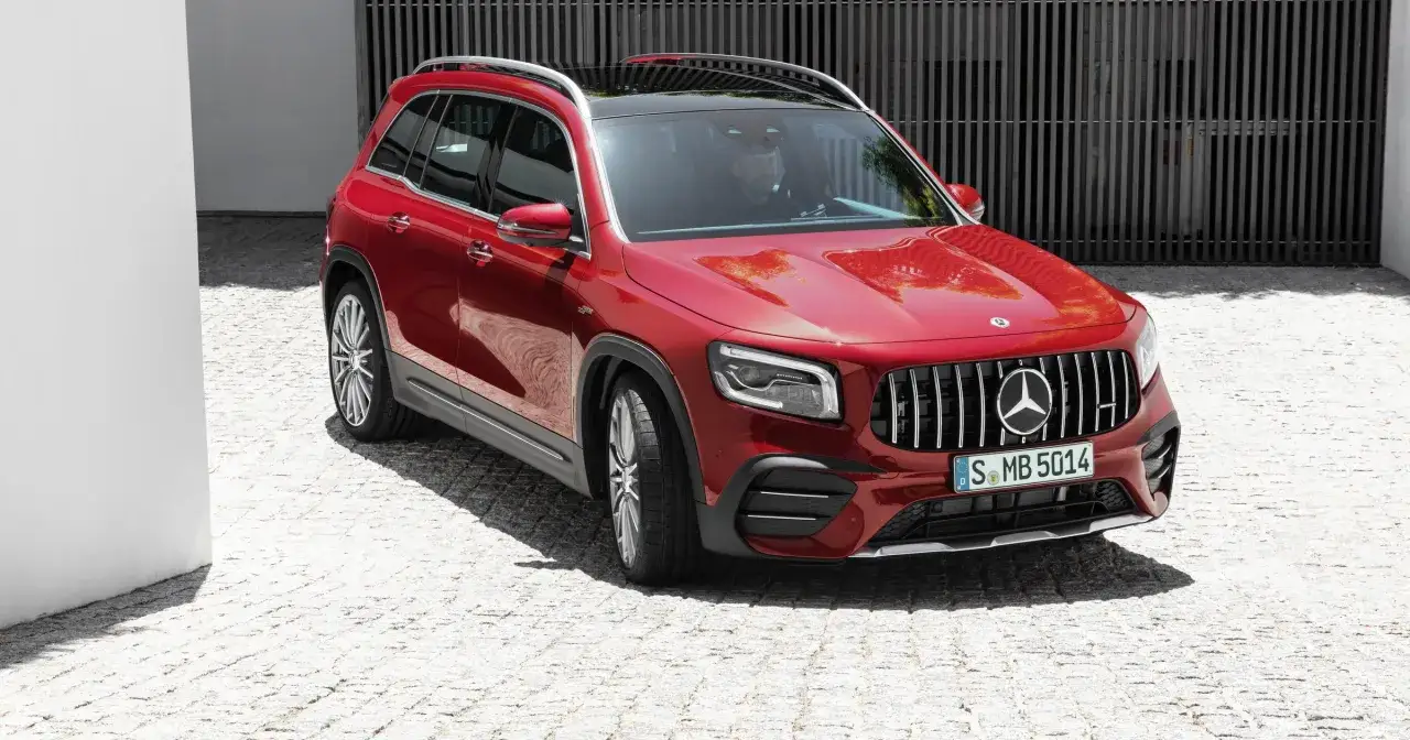Czerwony Mercedes 7 osobowy GLB AMG z kierowcą za kierownicą, zaparkowany na brukowanej nawierzchni.