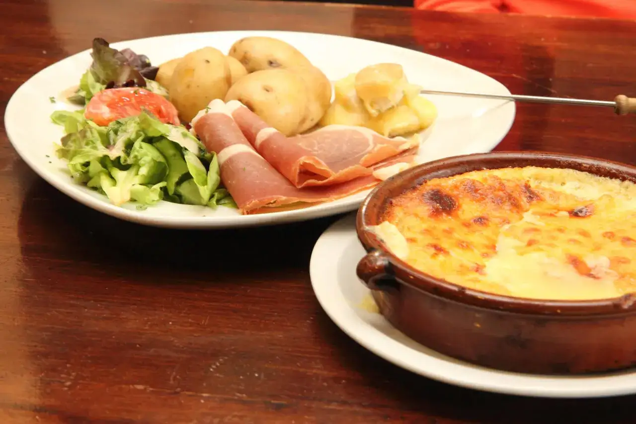Un plat de spécialités culinaires auvergnates : pommes de terre, jambon cru, salade et un gratin de fromage doré.