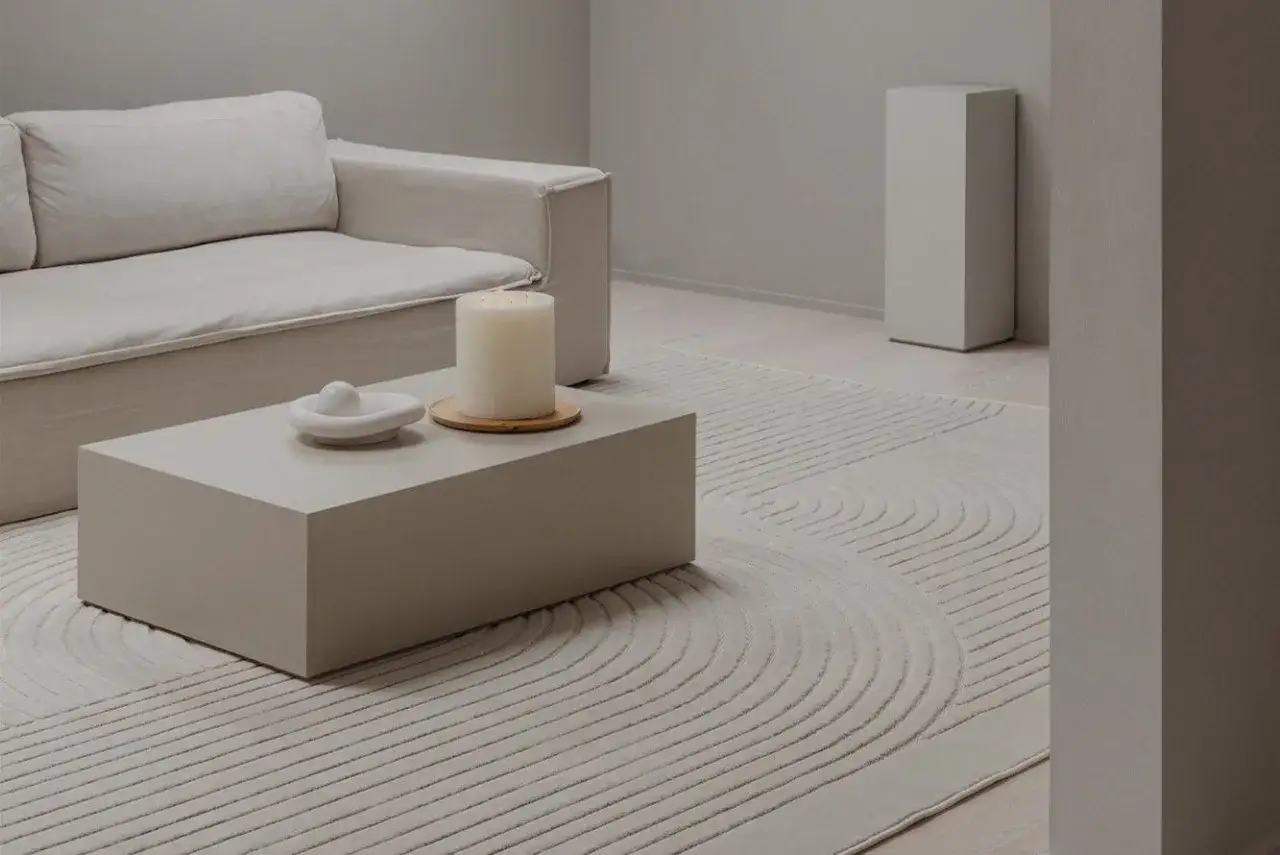 Salon w odcieniach ivory: sofa, stolik kawowy, świeca i dywan z geometrycznym wzorem tworzą spokojną aranżację.
