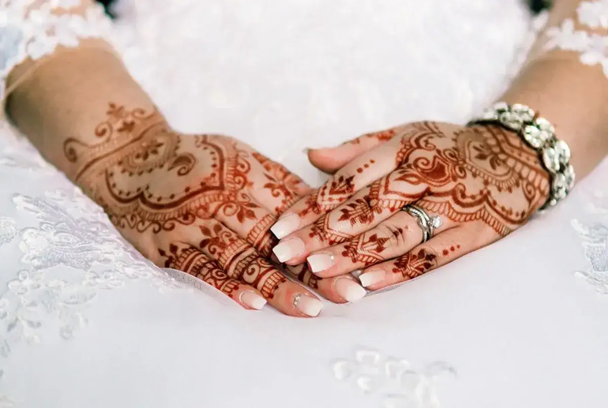Manos de novia con intrincados diseños de henna, anillos y pulsera brillante, listas para la boda.