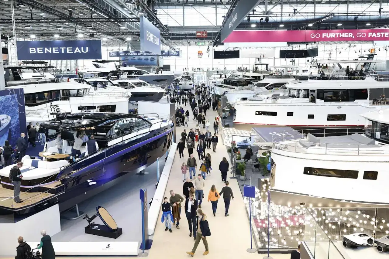 Besucher bestaunen Yachten auf einer Messe. Ein glänzendes, blaues Boot im Vordergrund erinnert an eine Fahrt auf dem kanal frankreich.