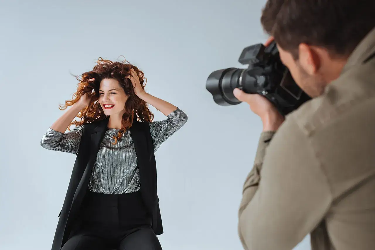 Modelka z burzą rudych włosów pozuje do zdjęcia. Fotograf robi jej zdjęcie. To sesja TFP, co to znaczy?