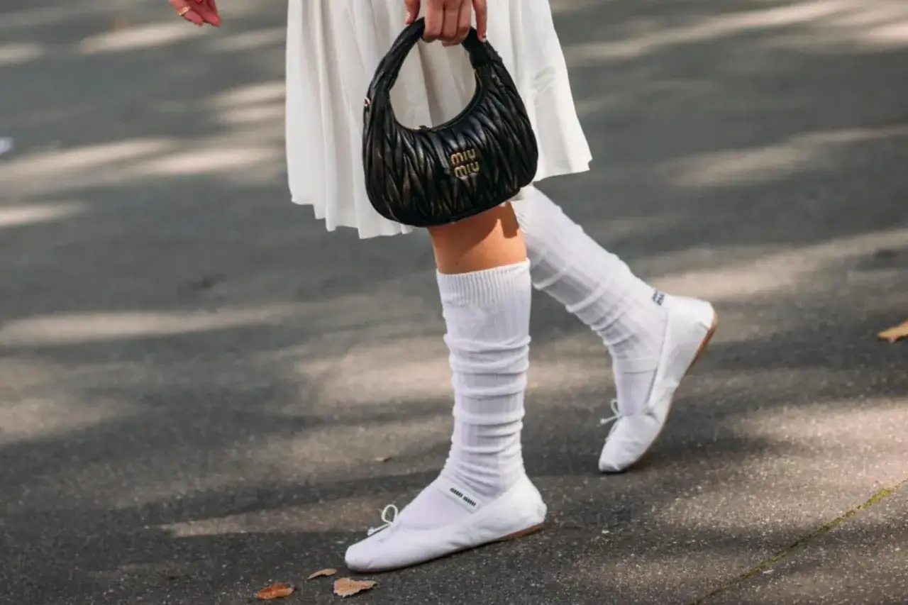 Piernas con bailarinas blancas y calcetines blancos arrugados, un look chic para bailarinas con calcetines.