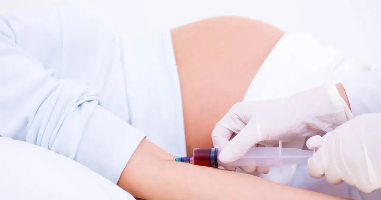 Pobieranie krwi do badań w 15 tygodniu ciąży. Lekarz w rękawiczkach pobiera krew strzykawką od ciężarnej.