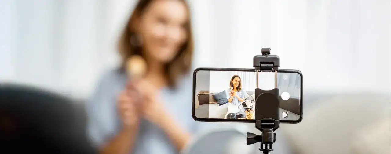 Kobieta nagrywa filmik telefonem komórkowym, trzymając pędzel do makijażu.