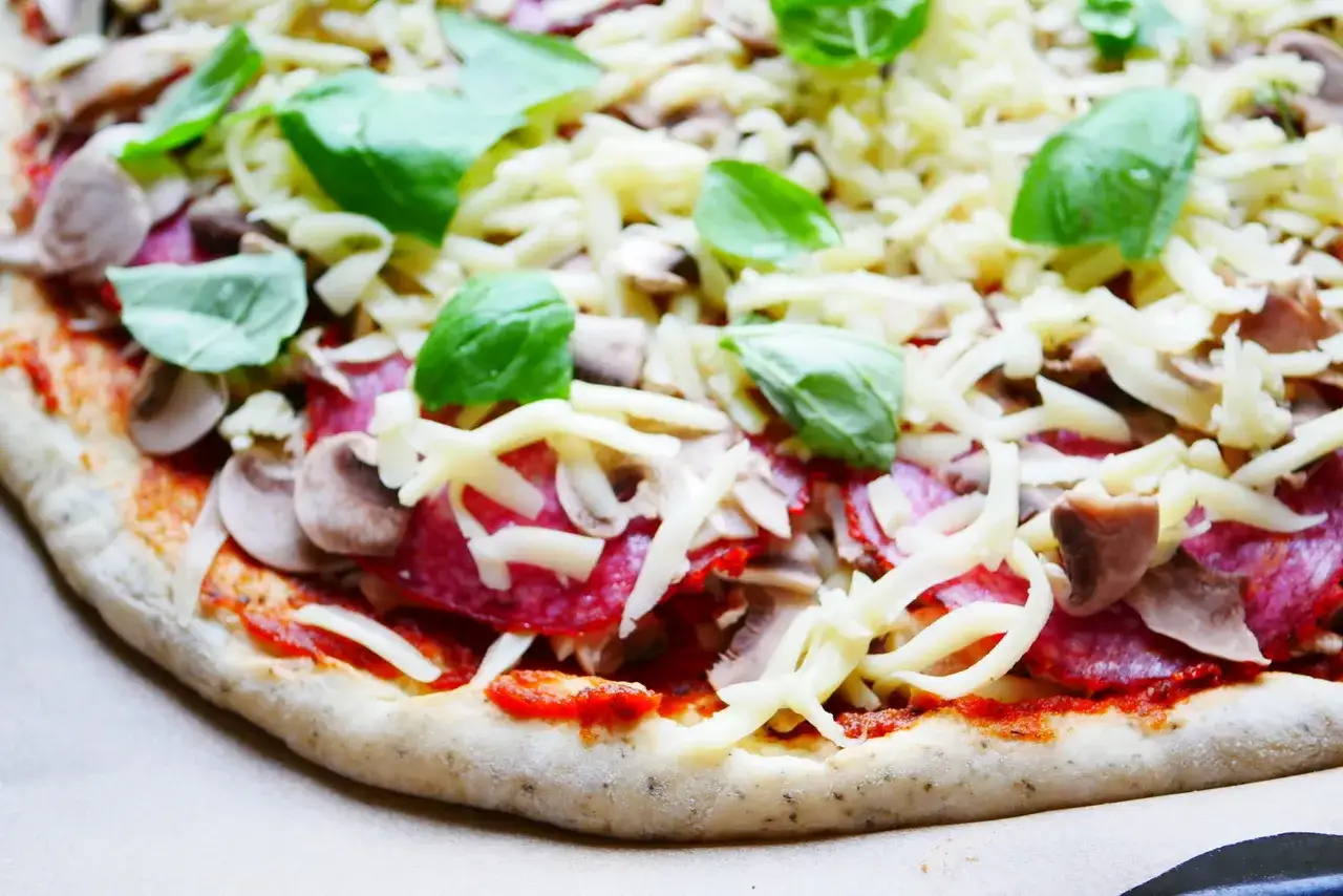 Gotowy do pieczenia przepis na ciasto do pizzy: sos pomidorowy, salami, pieczarki, ser i świeża bazylia.