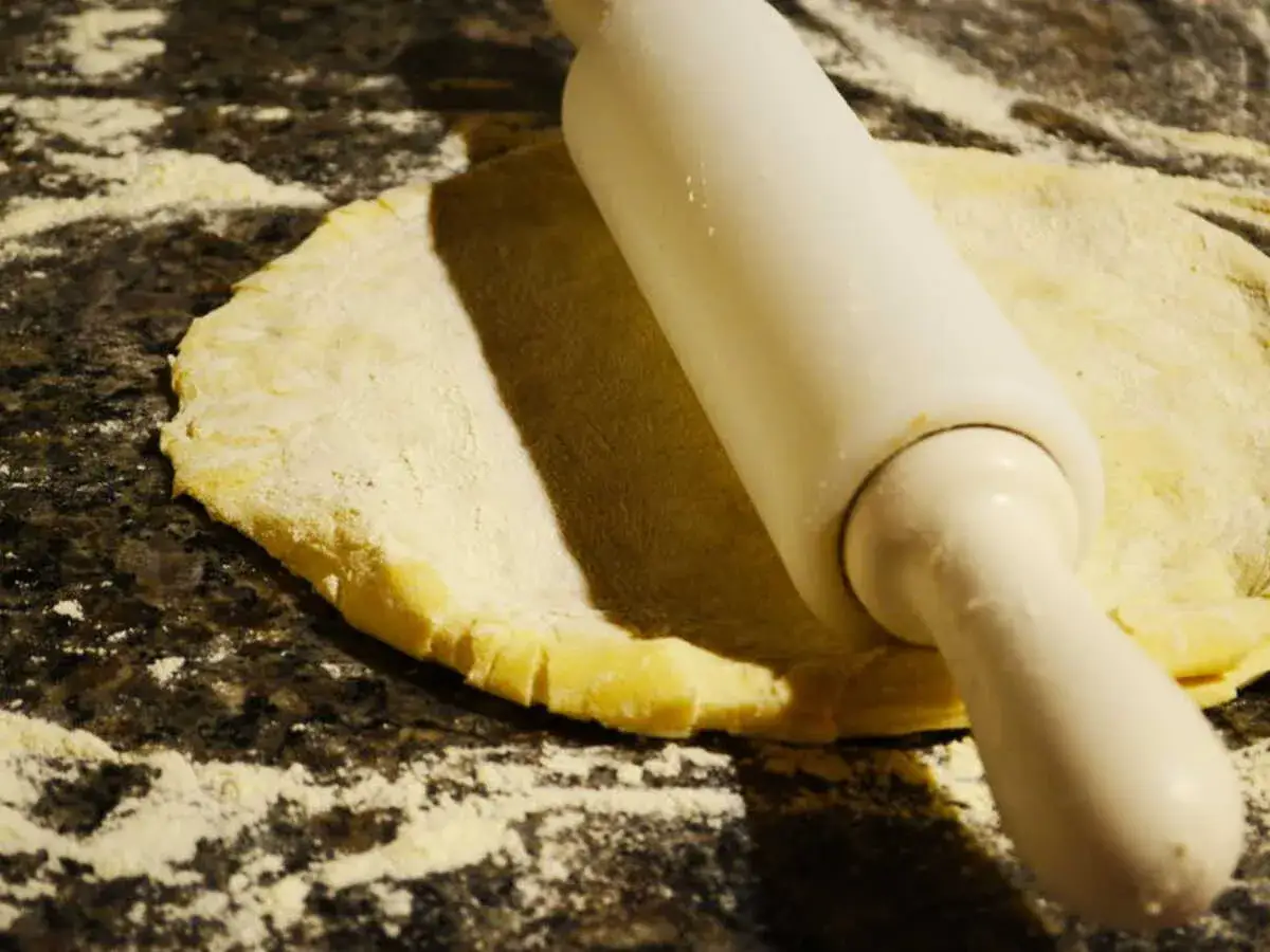 Rouleau à pâtisserie aplatissant une pâte à foncer sur un plan de travail fariné.