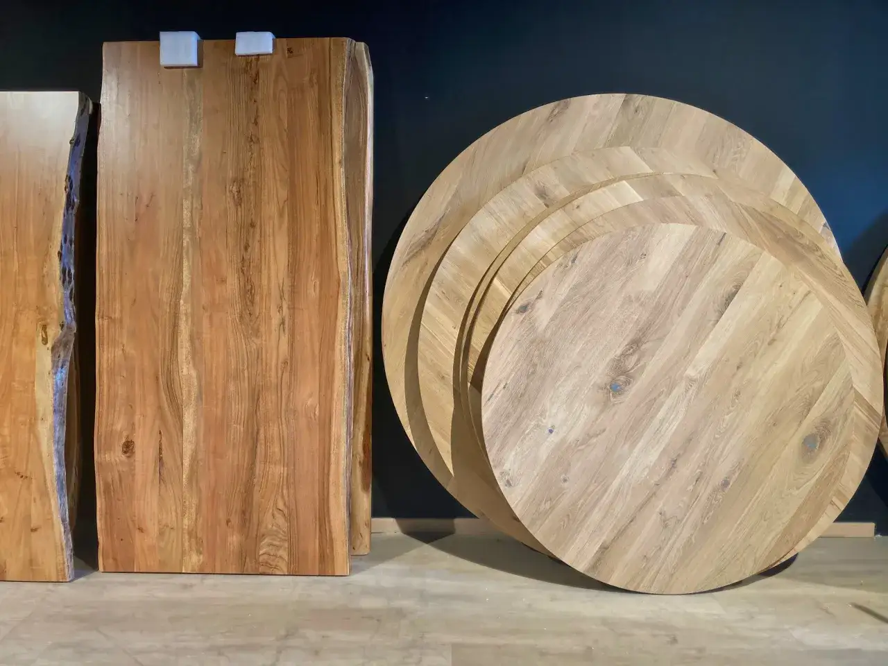 Plusieurs plateaux de table ronde en bois, empilés, illustrent la définition d'une table ronde. Des planches de bois brut sont aussi visibles.