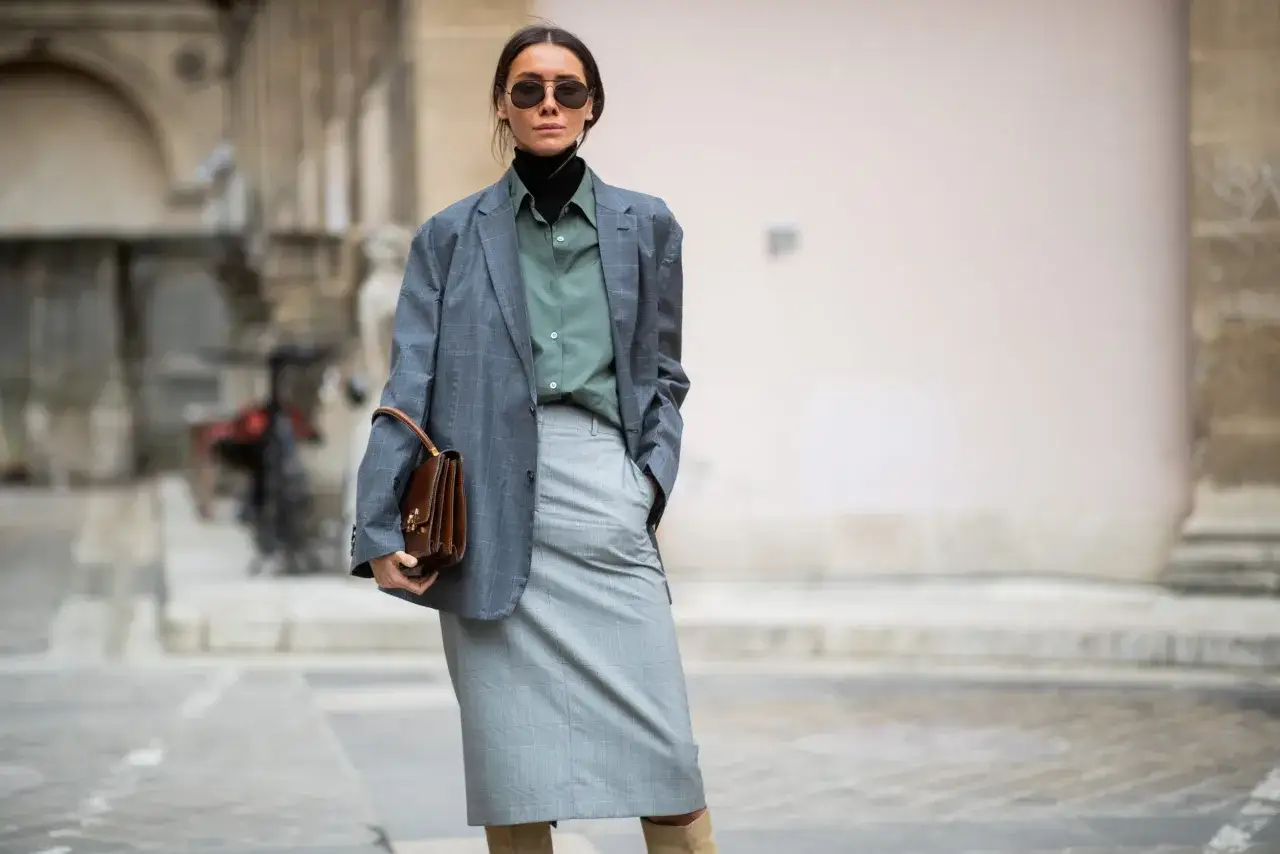 Elegancka stylizacja: szary garnitur, zielona koszula i czarny golf. Torebka dodaje klasy.