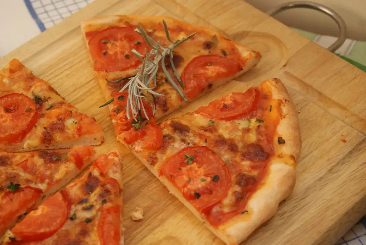 Kawałki pysznej pizzy bezglutenowej z pomidorami i rozmarynem na desce. Idealny przepis na pizzę bezglutenową.