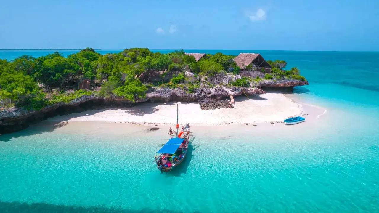 Rajska wyspa z chatkami i łodzią, idealne miejsce na Zanzibar na własną rękę. Turkusowa woda, biały piasek i bujna zieleń.