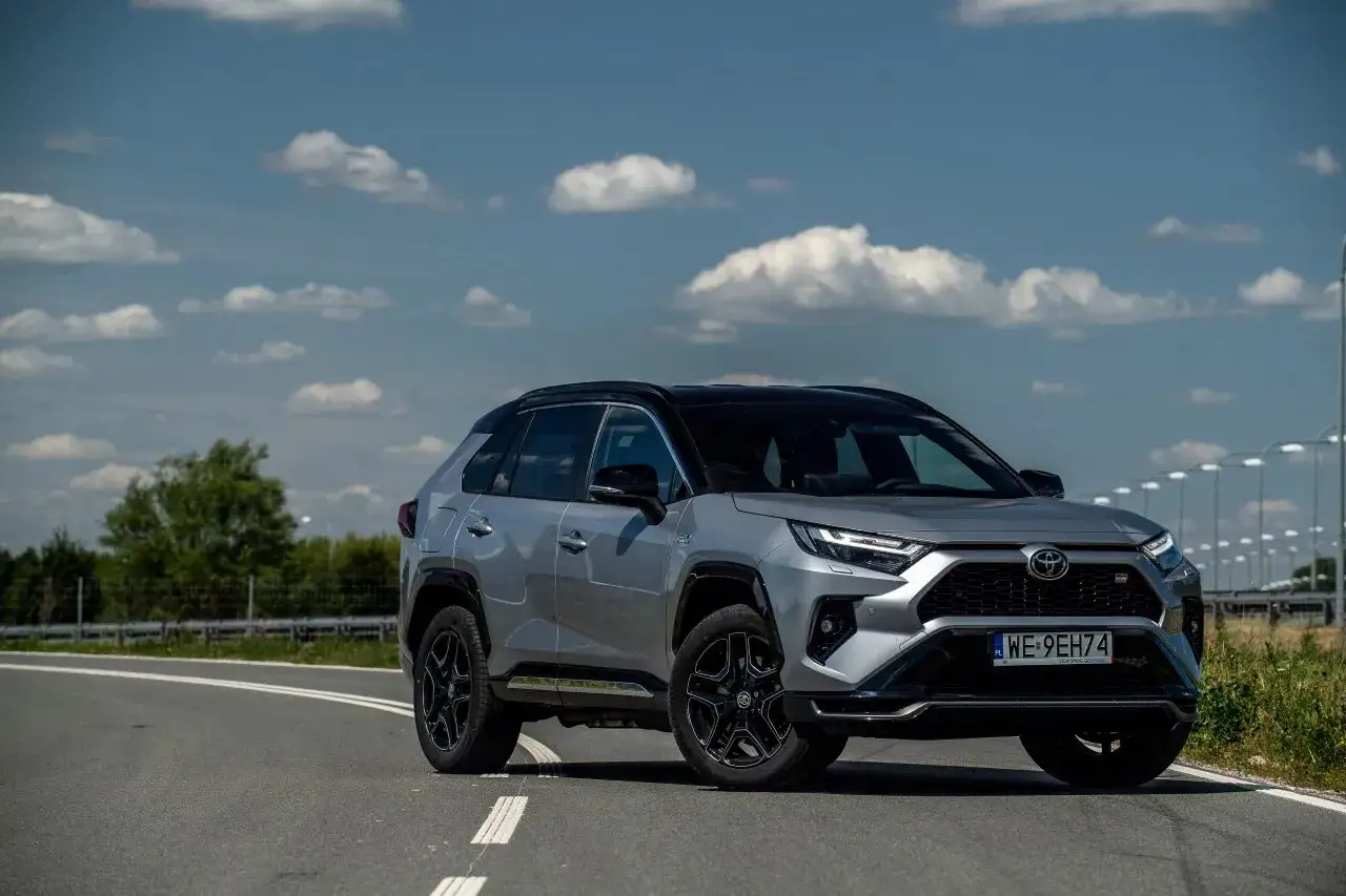 Srebrny SUV na drodze, z czarnym dachem. To jest plug in hybrid, co to znaczy? To połączenie silnika spalinowego i elektrycznego dla oszczędności.