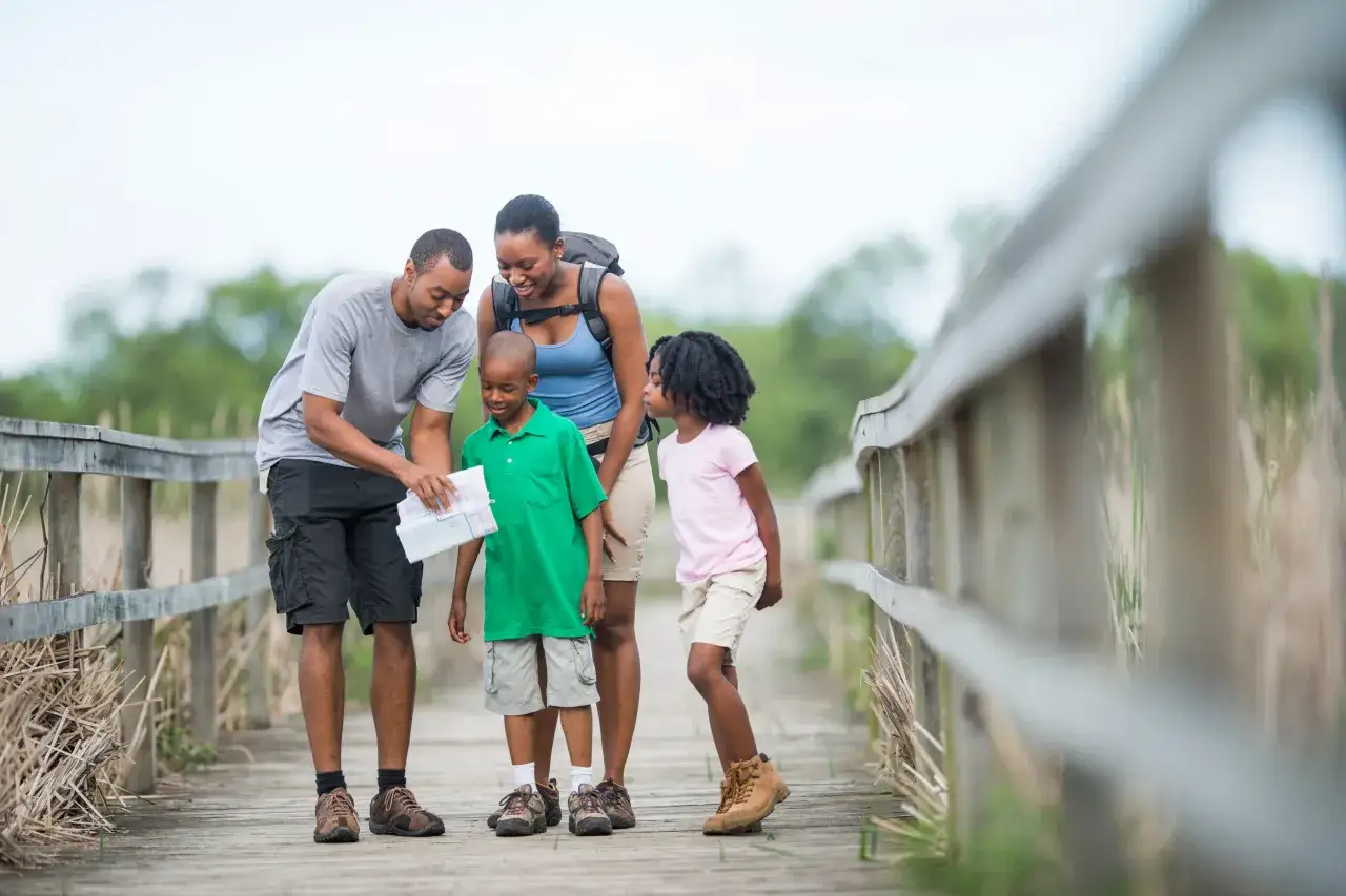 Rodzina na drewnianym pomoście, ojciec pokazuje dzieciom mapę. To piękny przykład tego, co **outdoor** to znaczy &ndash; wsp&oacute;lne odkrywanie natury.