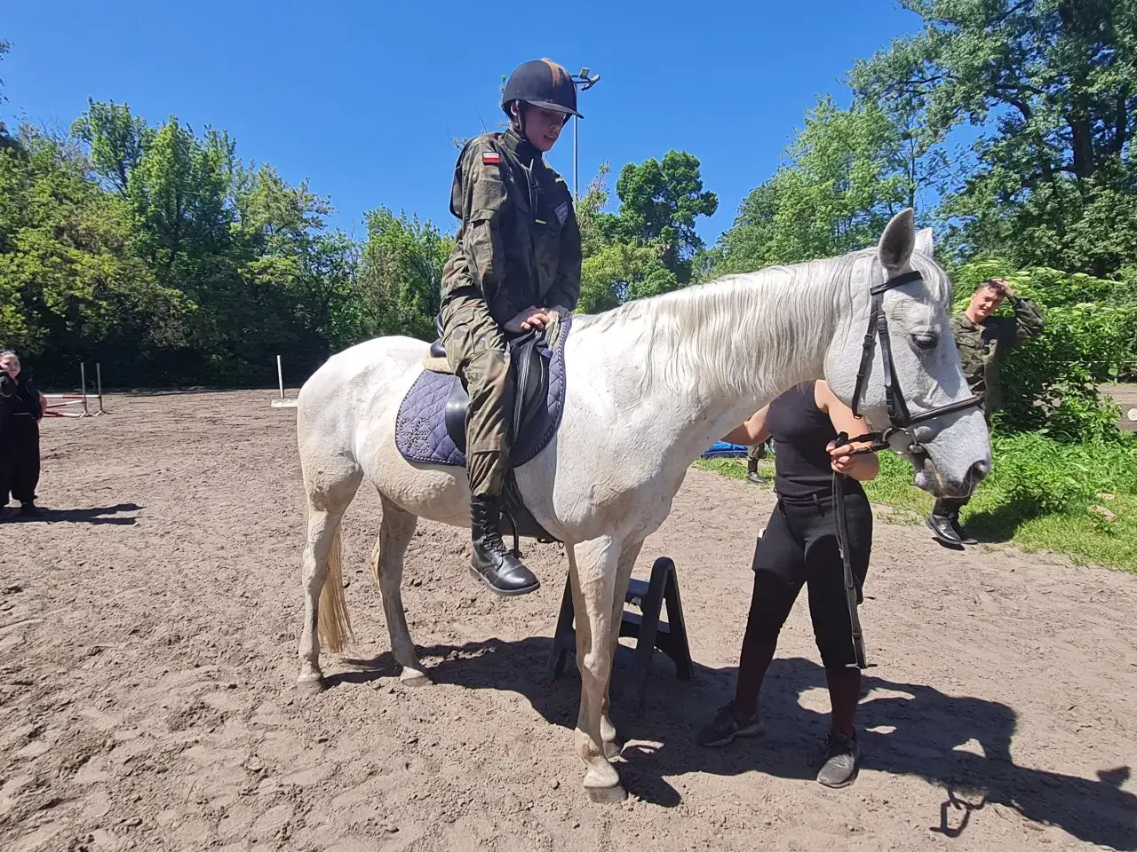 Młody jeździec w mundurze na białym koniu podczas treningu w stowarzyszeniu klub jeździecki Legia Kozielska.