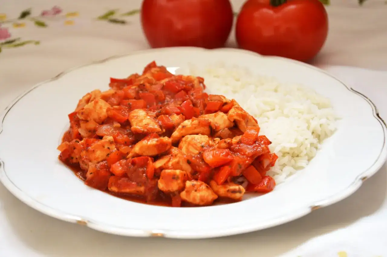 Ryż z warzywami i kurczakiem w sosie pomidorowym, podany na białym talerzu.