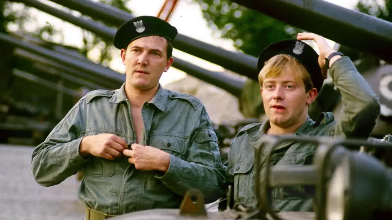 Dwóch żołnierzy w wojskowych mundurach i beretach. Jeden zapina koszulę, drugi poprawia beret. Scena z filmu 