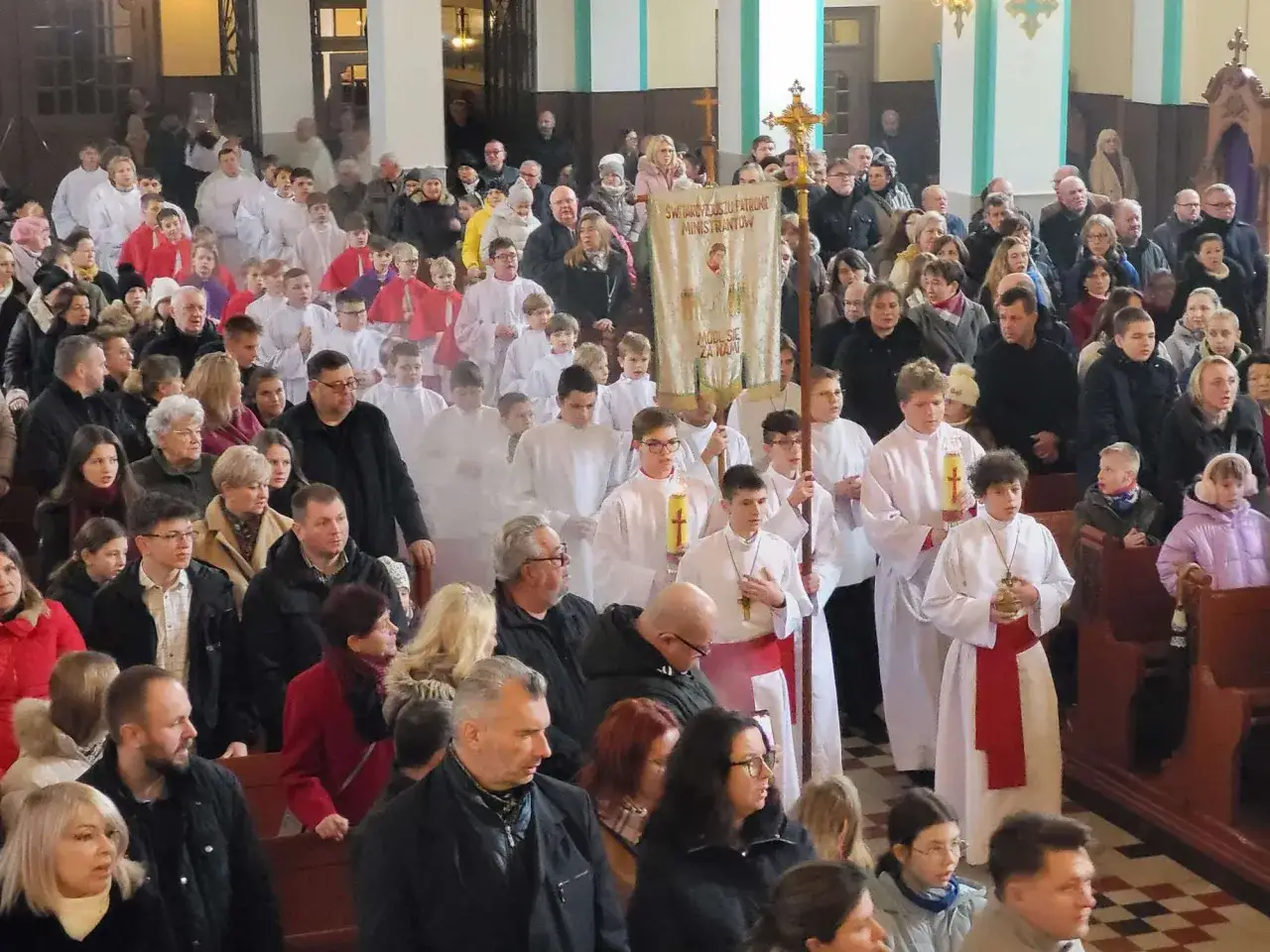 Dzieci w albach i ministranci niosący krzyż i sztandar podczas mszy. To jest msza suma, ważne wydarzenie dla parafii.