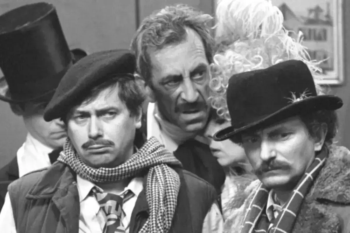 Aktorzy w kapeluszach i szalikach, w tym jeden w cylindrze, tworzą scenę z kabaretu Olgi Lipińskiej.