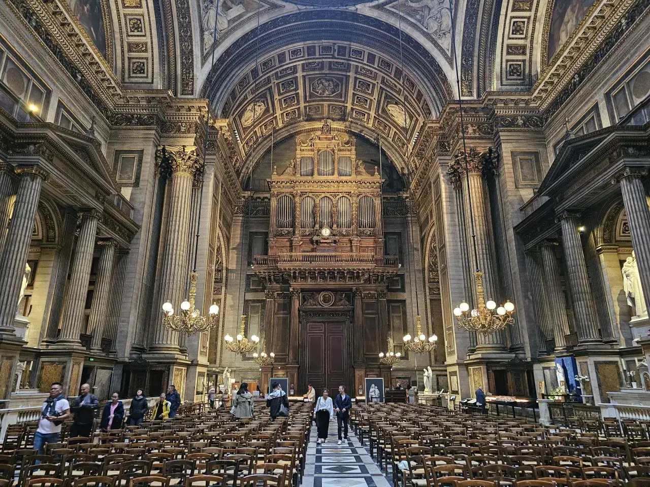 Wnętrze kościoła de la Madeleine w Paryżu, z imponującymi organami i rzędami krzeseł.